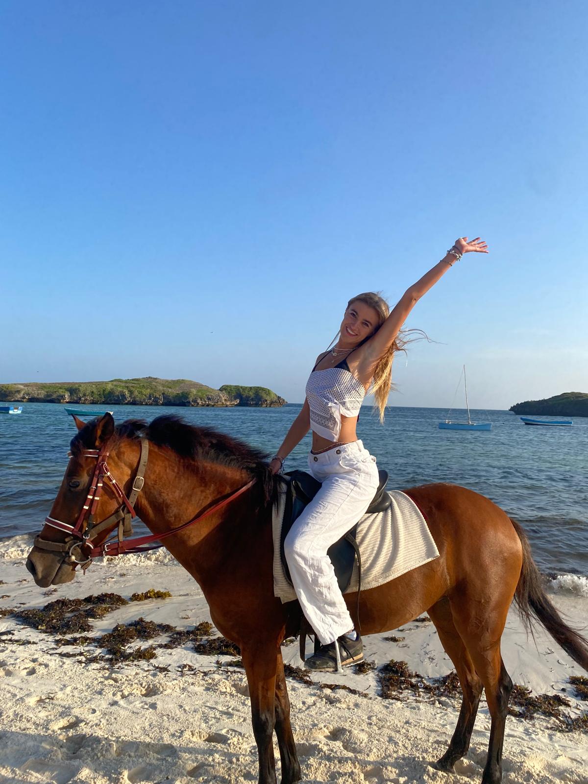 Young girl on a horse on a beach with her arm in the air and looking happy.